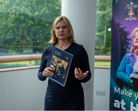 A woman holding a brochure stands in front of an advertising banner.